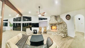 Een ruime woonkamer met een stenen open haard, comfortabele zitplaatsen en grote ramen.