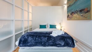 Une chambre moderne avec un grand lit, des murs blancs, un tableau et des panneaux de verre dépoli.
