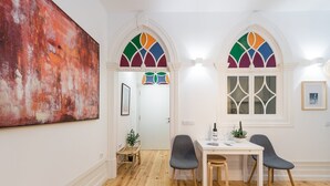 Un coin repas avec un plancher en bois, deux chaises grises, une table blanche et un vitrail coloré.