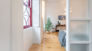 Un couloir avec un plancher en bois, une plante en pot, une petite table avec une chaise et un téléviseur fixé au mur.