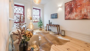 Une pièce chaleureuse avec un plancher en bois, une grande peinture abstraite, une table ornée d’un vase et de bougies, et un luminaire original.