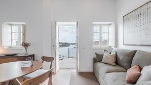 Un salon moderne avec un canapé, une table à manger et des chaises, et une vue sur la mer par une porte ouverte.