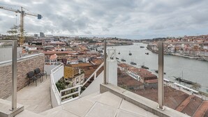 Un point de vue élevé surplombant une ville, avec une rivière, et offrant une vue sur un mélange de bâtiments résidentiels et commerciaux, un pont et un système de téléphérique.