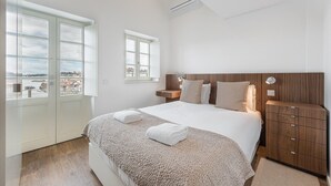 Une chambre avec un grand lit, une tête de lit en bois, des lampes de chevet, une table de chevet et une vue sur la ville par la fenêtre.