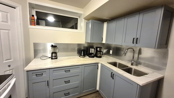 A kitchen with grey cabinets, a built-in window, a sink, and a coffee maker.