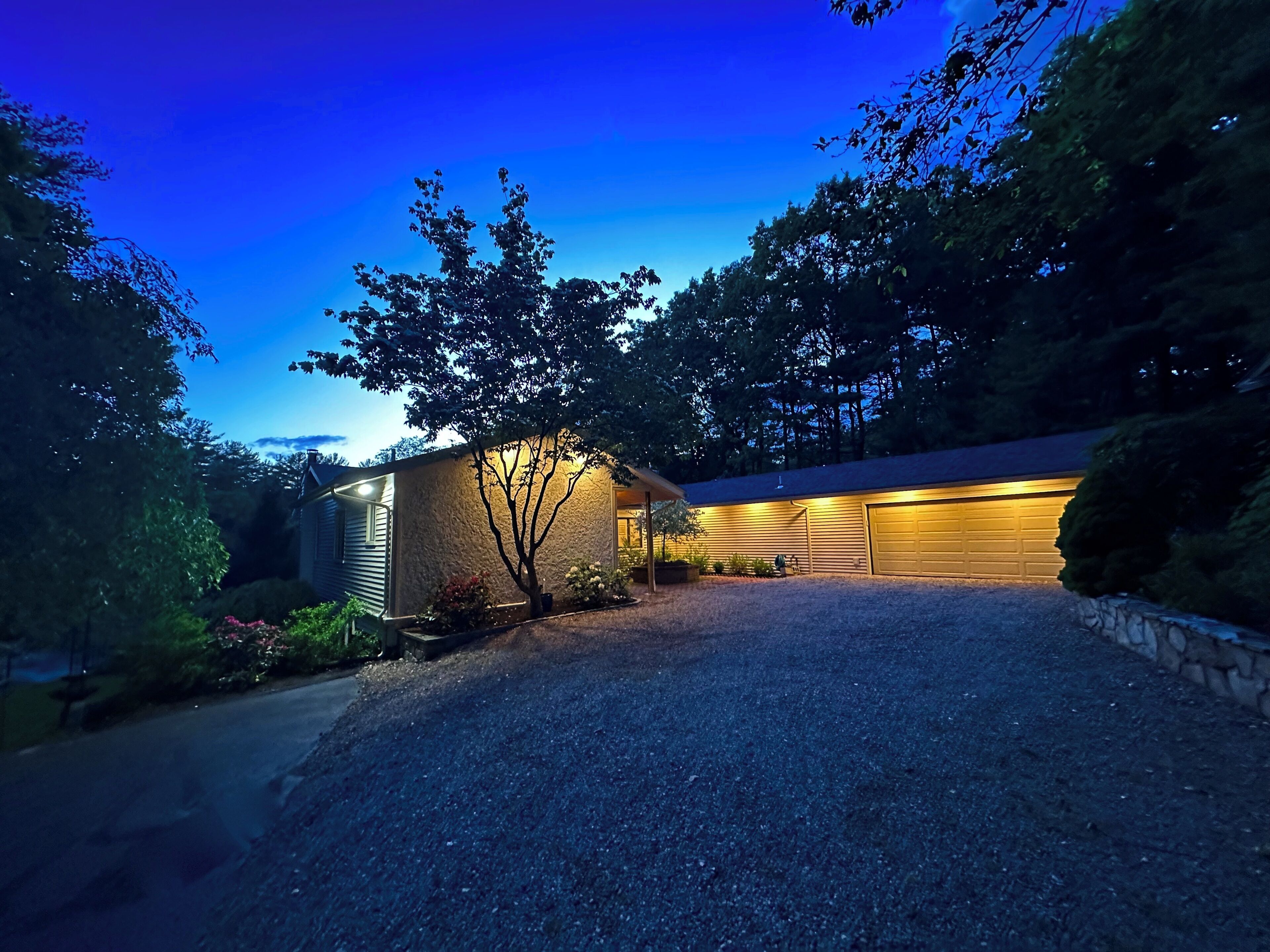 Une maison moderne avec un garage, entourée d’arbres et dotée d’une allée gravillonnée.