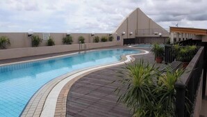 A swimming pool with a wooden deck, surrounded by potted plants and a building with a sloped roof. - Natol Homestay-Riverbank Suites High Rise City Centre (Kuching)