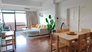 A modern living room with a dining area, large windows, and a plant. - Natol Homestay-Riverbank Suites High Rise City Centre (Kuching)