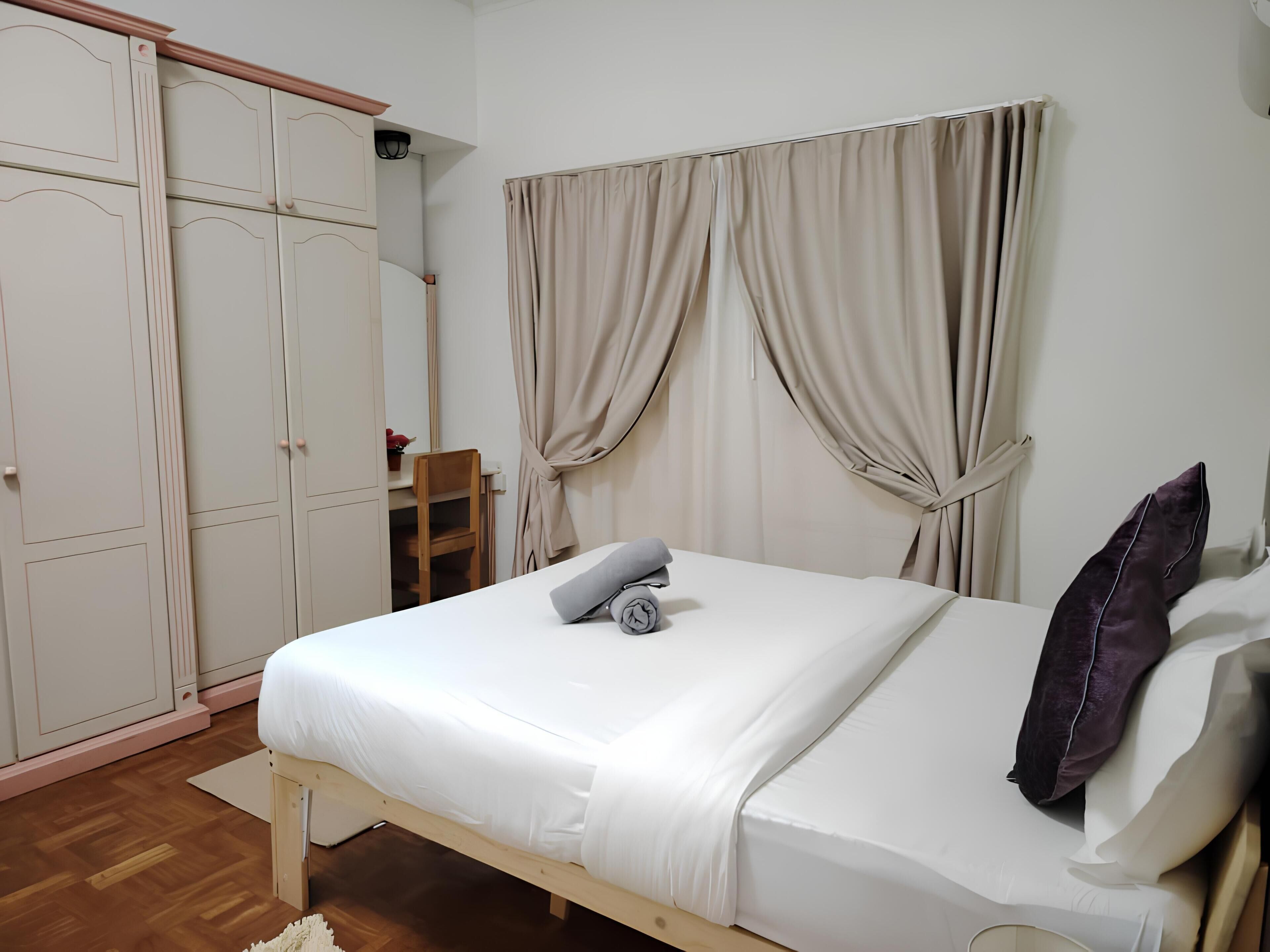 Ein Schlafzimmer mit einem Bett, einem Holzstuhl, einem Kleiderschrank und beigen Vorhängen.