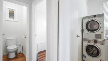 Ett tvättrum med en tvättmaskin och en torktumlare placerade ovanpå varandra, en toalett och ett litet fönster.