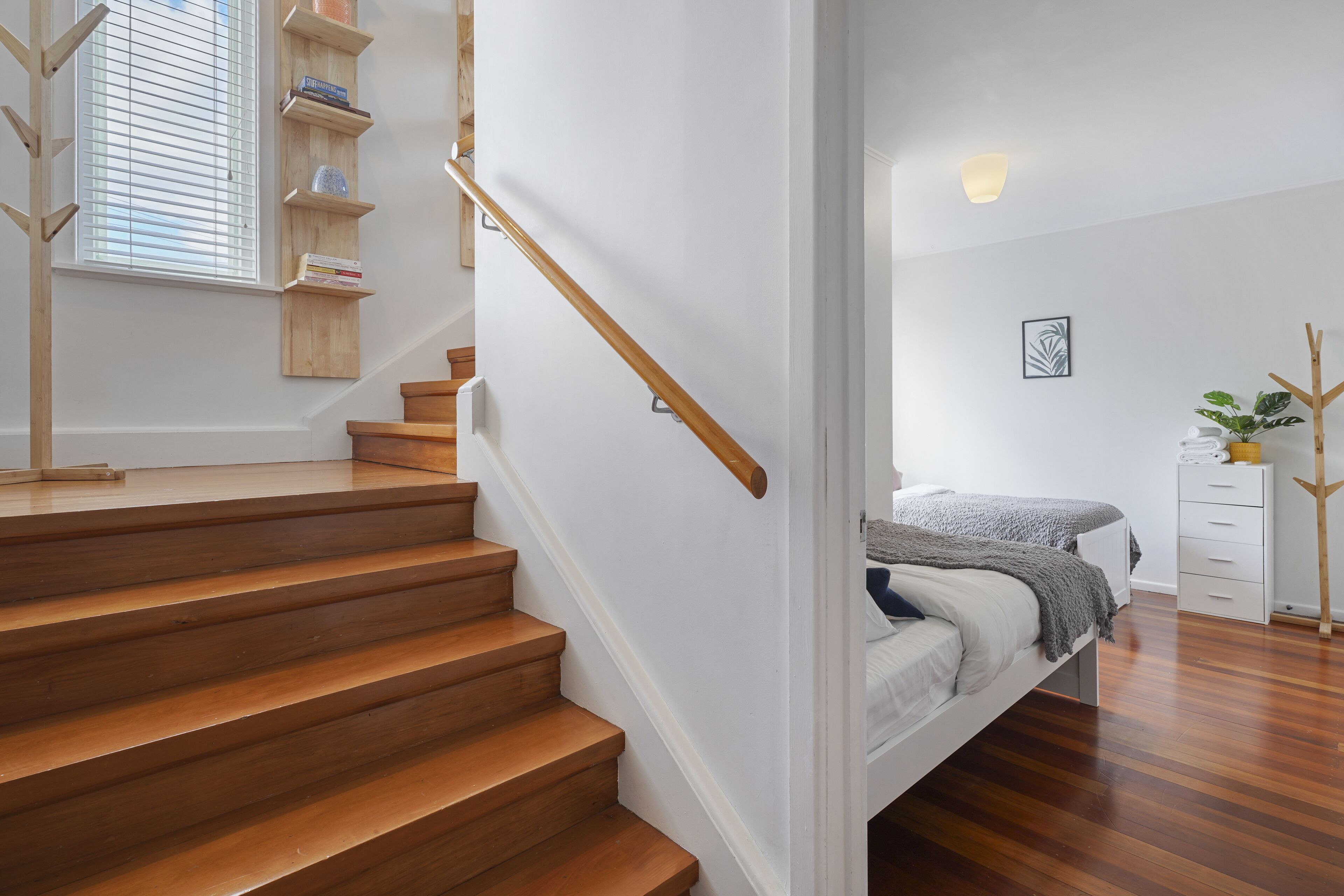 A modern bedroom with a wooden staircase, a bed with a gray blanket, a bedside table, and a nightstand.