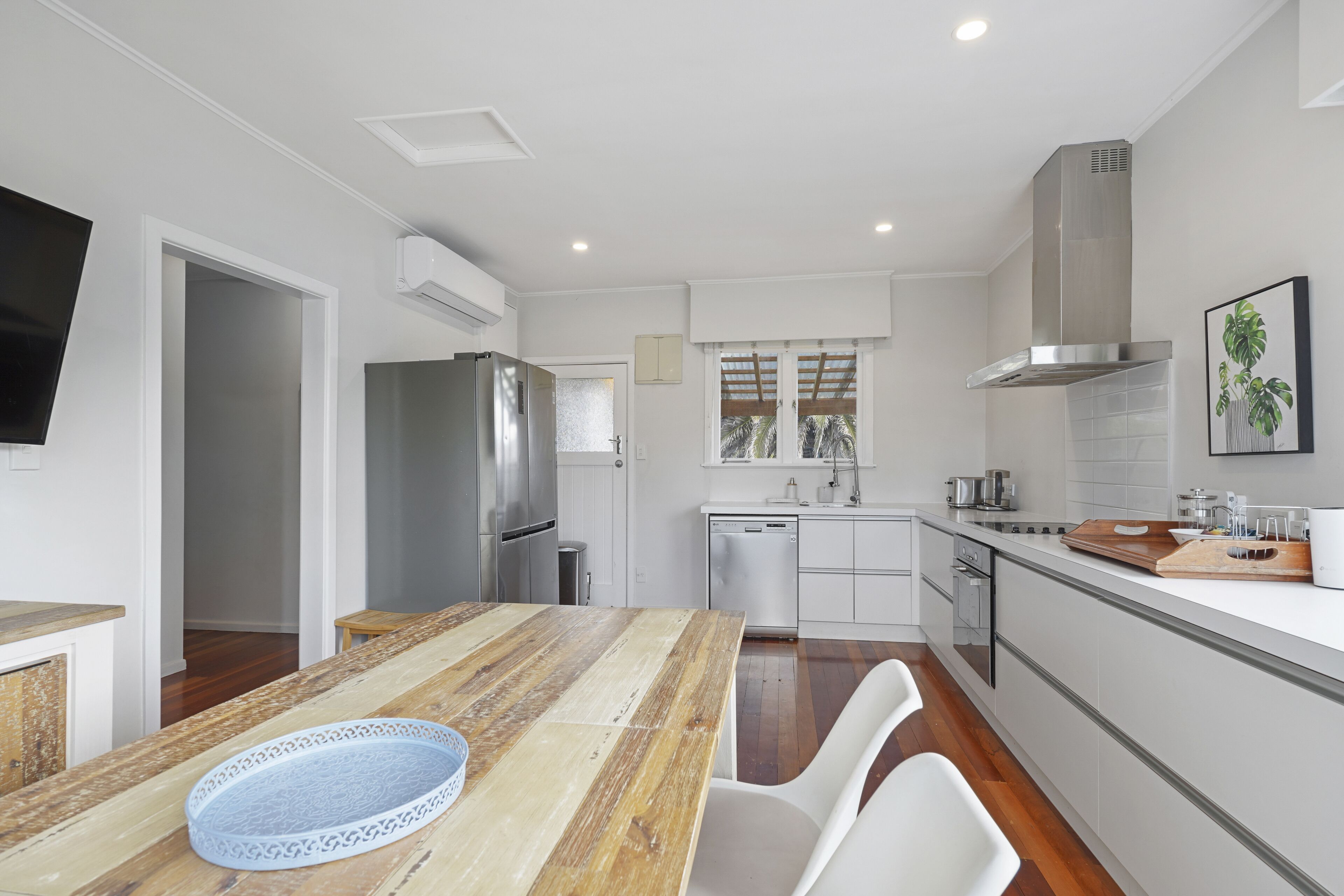 A modern kitchen with a wooden dining table, white chairs, a stainless steel refrigerator, and a built-in oven.
