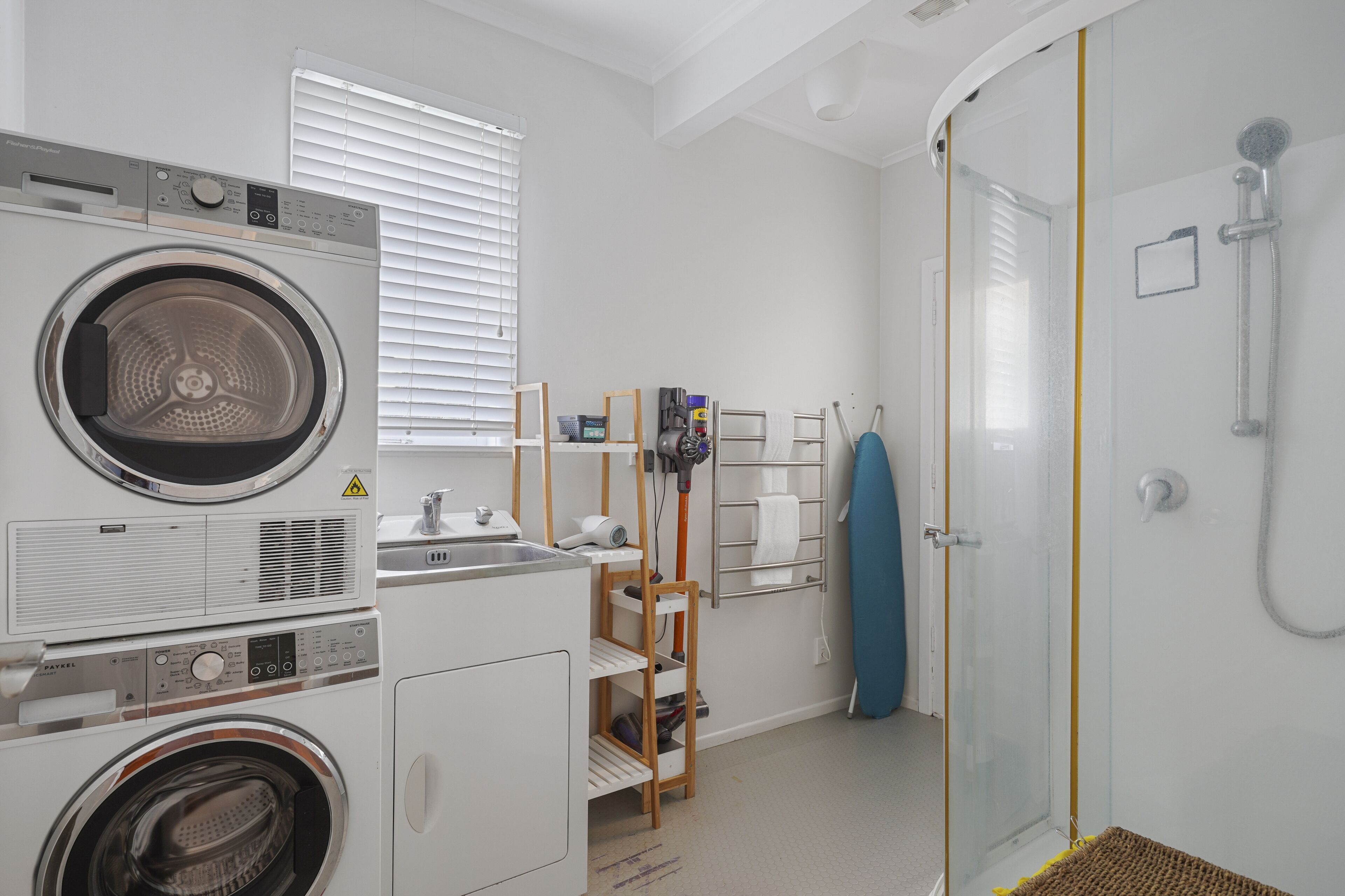 A laundry area with a front-loading washer and dryer, a drying rack, and a shower enclosure.