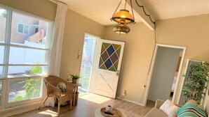Uma sala de estar ampla com uma grande janela, uma poltrona de vime, um sofá e um lustre.