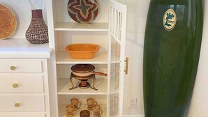 A room with a white cabinet containing kitchenware, a surfboard, and decorative items.