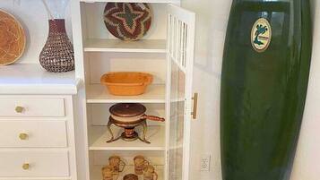 A room with a white cabinet containing kitchenware, a surfboard, and decorative items.
