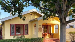 A yellow house with a number '525' on the wall, a porch with chairs, and a tree in the foreground.