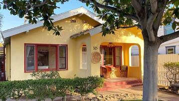 A yellow house with a number '525' on the wall, a porch with chairs, and a tree in the foreground.