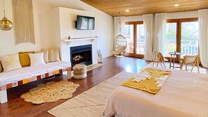 Un dormitorio amplio con una cama grande, chimenea, televisor y un balcón con mobiliario de exterior.