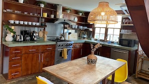 A kitchen with wooden cabinets, a stove, and a dining table with yellow chairs. - Indah Jungalow Moonlight, Downtown Encinitas CA (Encinitas)