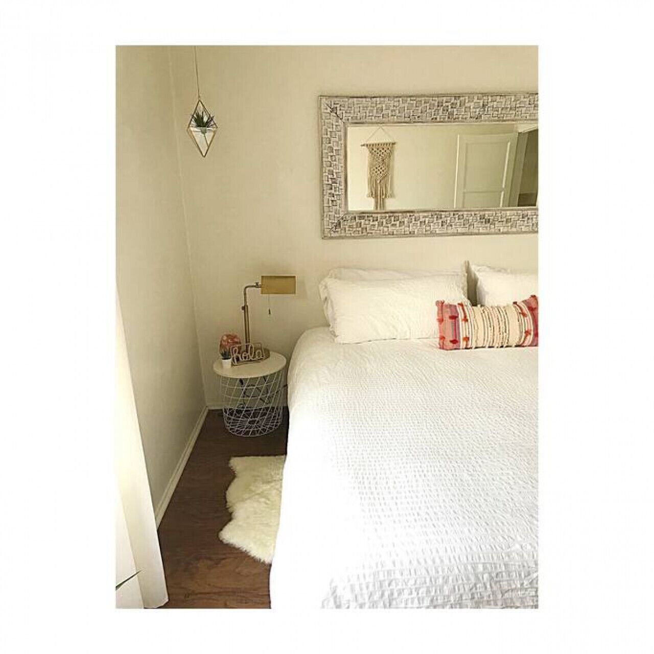 Un dormitorio con una cama grande, una mesita de noche, una lámpara, un espejo y una planta colgante.