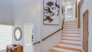 A staircase with wooden steps and a metal handrail, leading to a landing with a large abstract painting and a mirror.