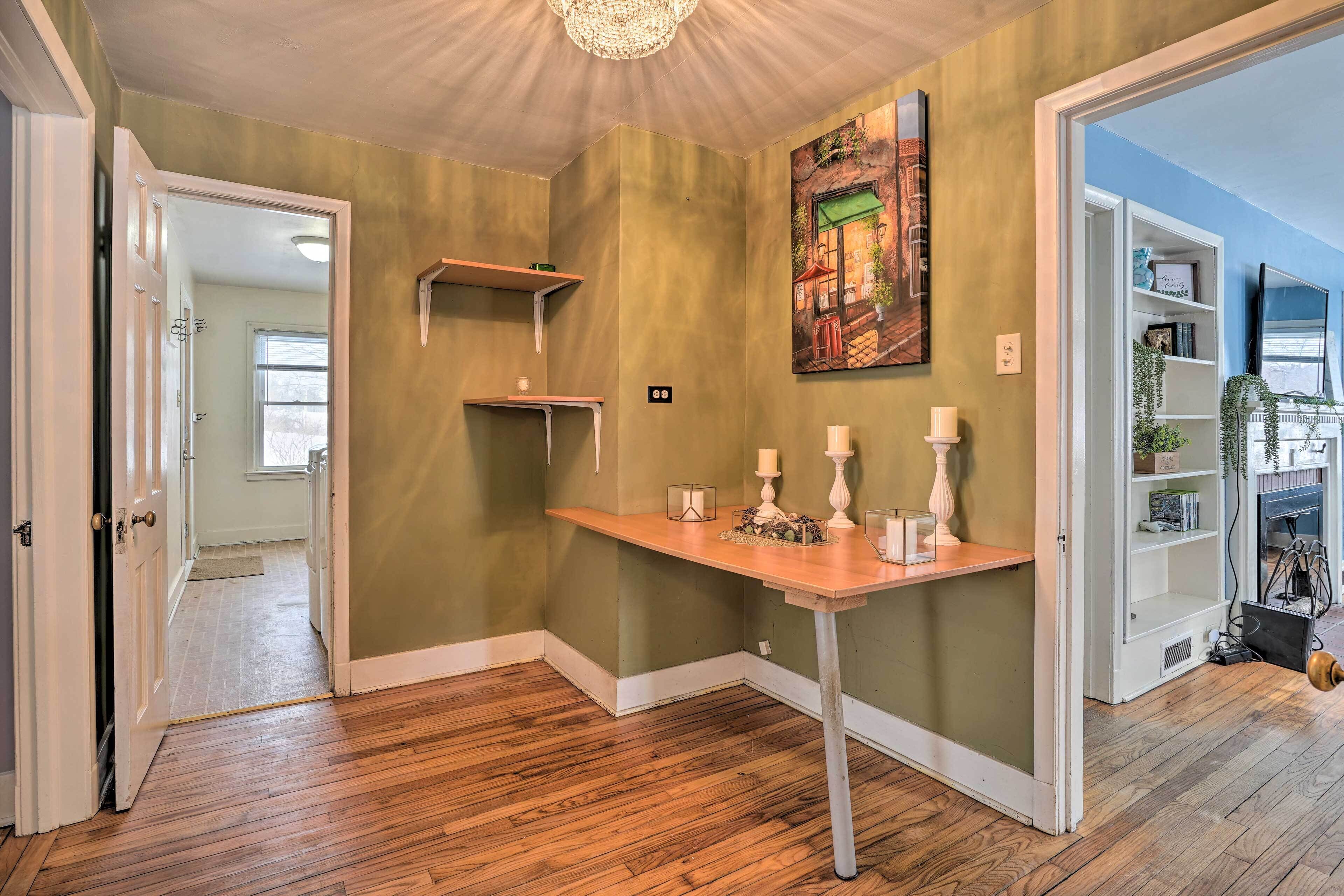 A hallway with wooden flooring, a white door, a small table with candles, and a bookshelf with plants.