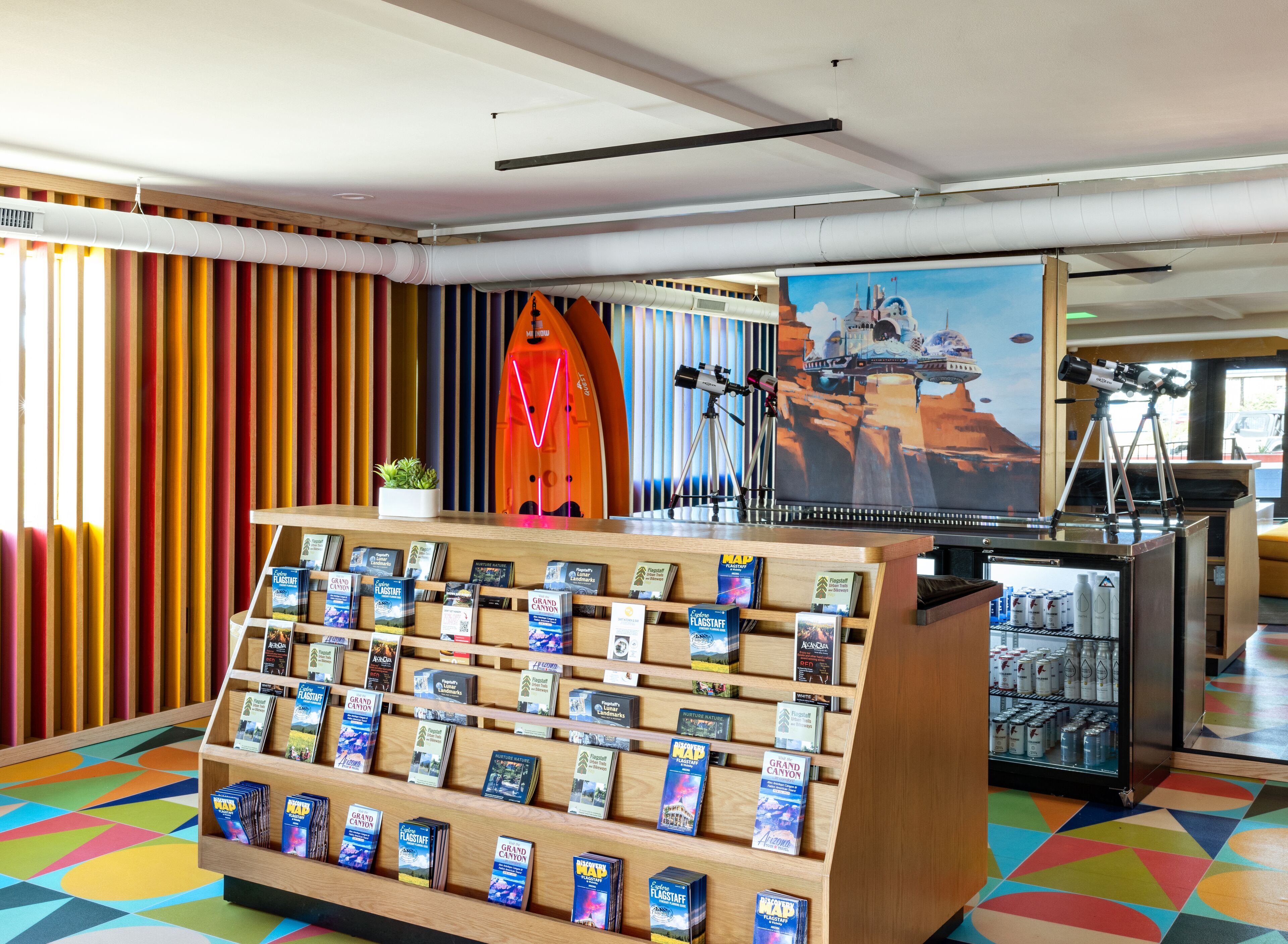 A travel information desk with a display of maps and brochures, a surfboard, and a telescope.