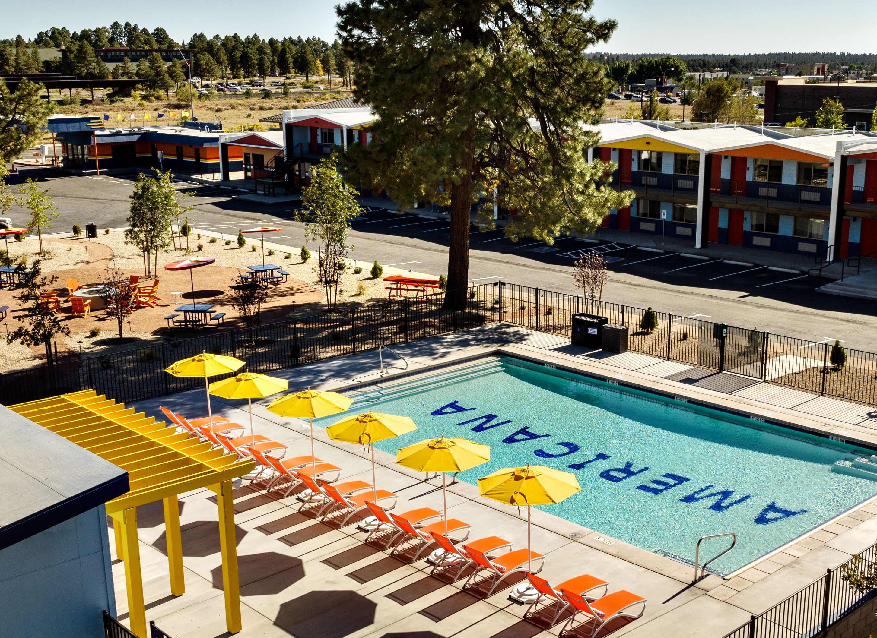 A swimming pool with 'AMERICAN' written on the water, surrounded by orange lounge chairs and yellow umbrellas.