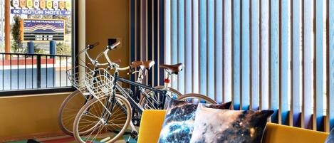 Une pièce avec un canapé jaune, un vélo et une fenêtre donnant sur une enseigne où l’on peut lire « AMERICANA MOTOR HOTEL ».