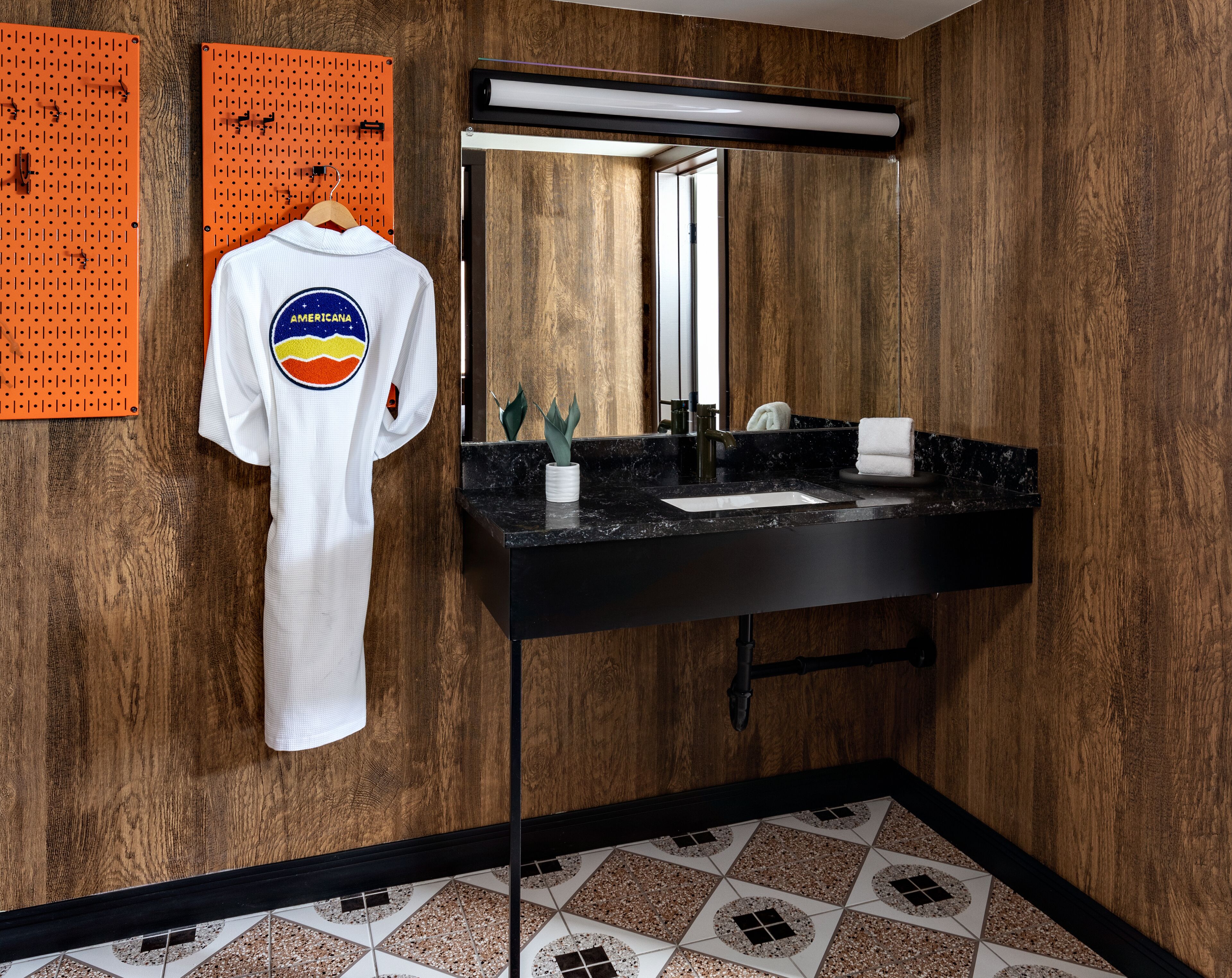 Un baño moderno con un lavamanos negro, paredes de madera, un espejo y un perchero con una bata blanca.