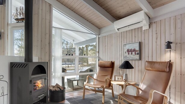 Un cuarto acogedor con estufa de leña, sillones de cuero, una mesa y un amplio ventanal con vistas al exterior.