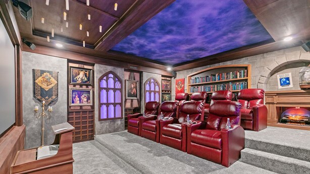 Una sala de cine en casa con sillones reclinables de cuero rojo, una estantería y una chimenea.