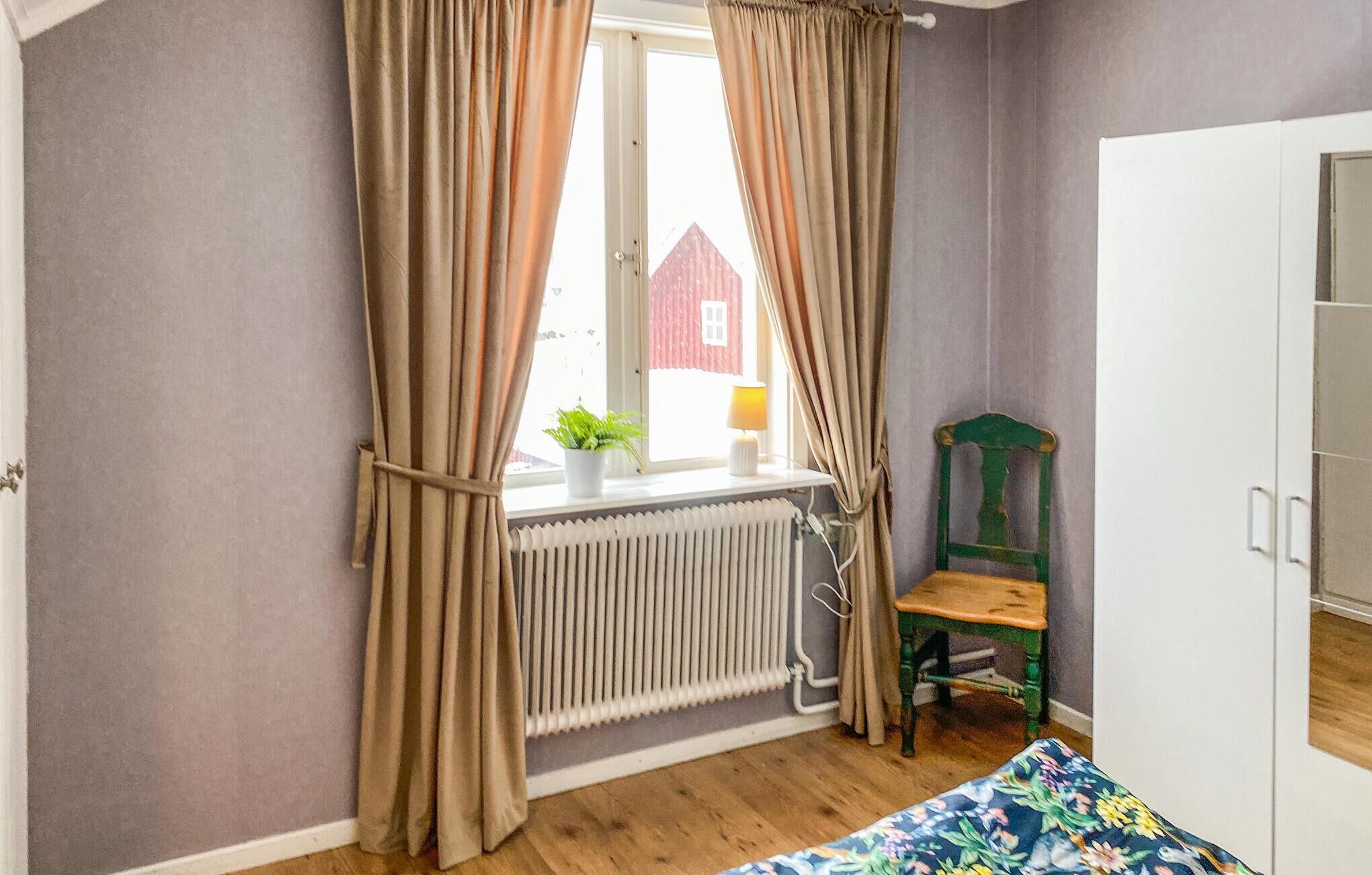 A bedroom with a window, radiator, chair, and bed.