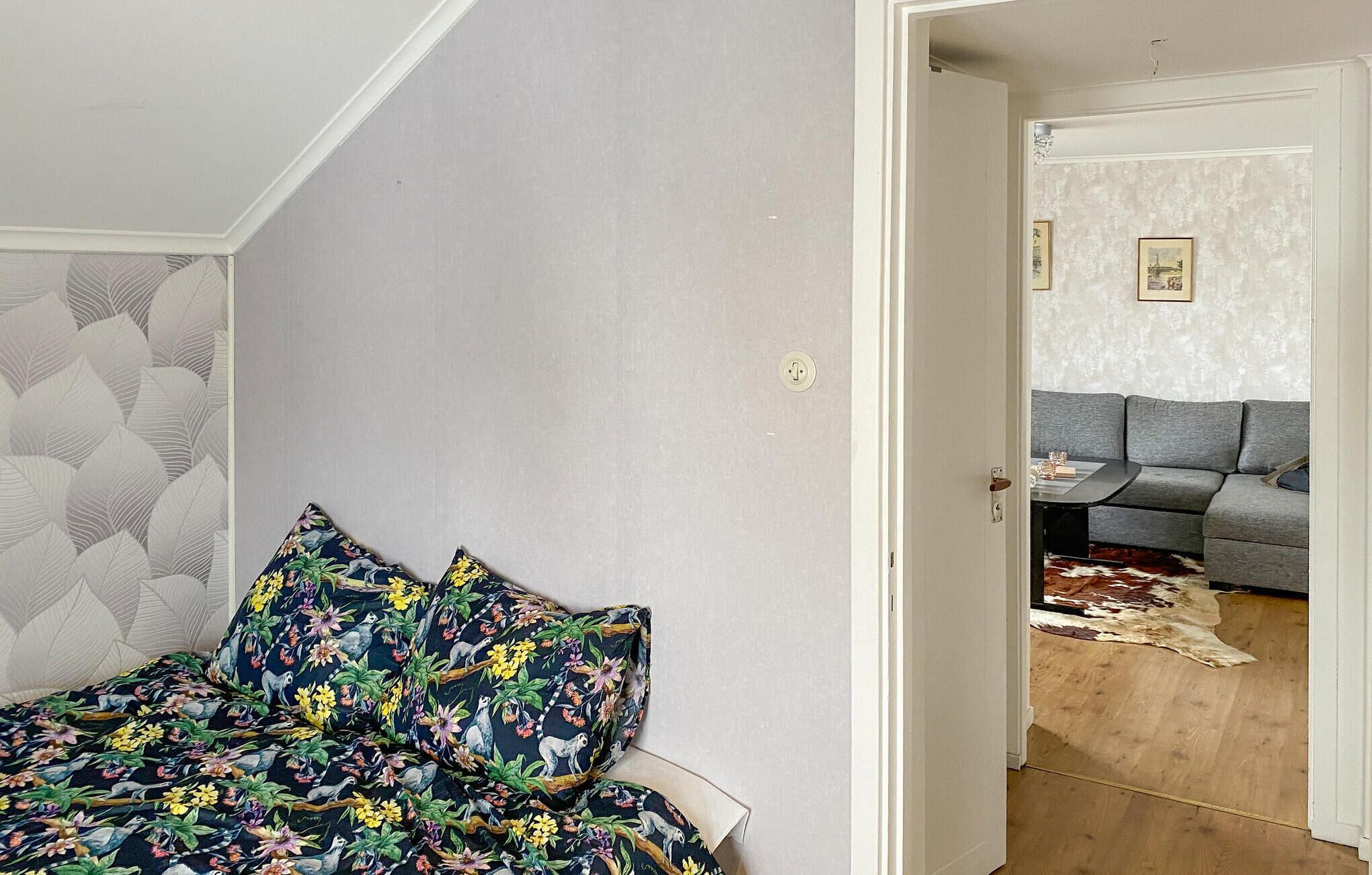 Ein Schlafzimmer mit einem Bett, einem gemusterten Kissen, einer Tür zu einem Wohnbereich mit einer Couch und einem Teppich.