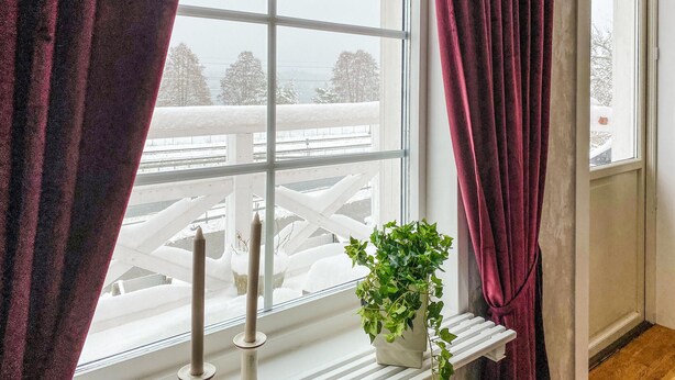 Ein Fenster mit Blick auf eine verschneite Landschaft, ein weißer Heizkörper und ein Blumentopf.
