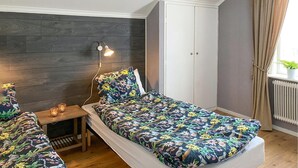 Ein Schlafzimmer mit einem Bett, Nachttisch, Lampe, Kleiderschrank und einem Fenster mit Vorhängen.
