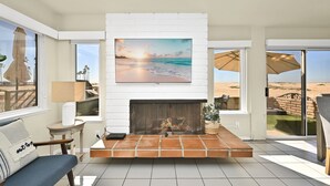 Una sala de estar con chimenea blanca, un televisor grande y vista a la playa.