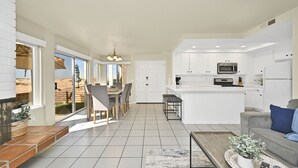 Una cocina moderna con armarios blancos, una isla central y una zona de comedor con una mesa grande y sillas.