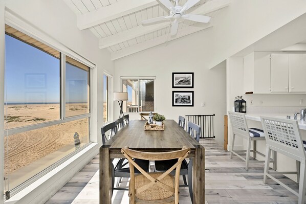 Un vaste espace dédié à la salle à manger, avec une grande table, des chaises et une vue sur la plage grâce à de grandes fenêtres.