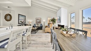 A spacious living area with a high ceiling, a dining table with chairs, a sofa, and a large window offering a view of the beach. - Beachfront home with Sweeping Ocean Views, AC, Walk to the Pier, Restaurants, Shops, Activities (Newport Beach)