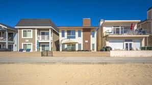 A beachfront hotel with a sandy beach in front, a two-story structure with a balcony, and a visible garage. - Oceanfront Home on the Boardwalk w/ 3 car Garage, AC, Giant Patio, Ocean Views, Walk to Pier (Newport Beach)