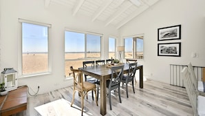 A dining area with a wooden table and chairs, large windows with a beach view, and a ceiling fan. - Oceanfront Home on the Boardwalk w/ 3 car Garage, AC, Giant Patio, Ocean Views, Walk to Pier (Newport Beach)