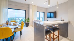 A modern kitchen with a central island, large windows, and a dining area with yellow chairs.
