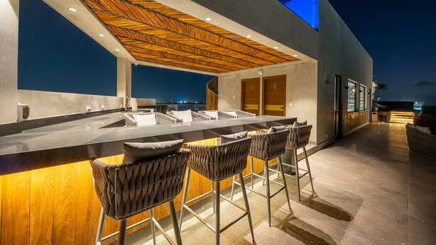 An outdoor bar area with a modern design, featuring a wooden ceiling, bar stools, and a long counter.