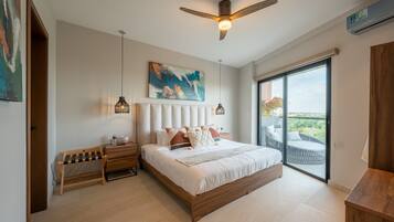 Un dormitorio moderno con una cama grande, un ventilador de techo, un cuadro y vistas a través de un ventanal corredero.