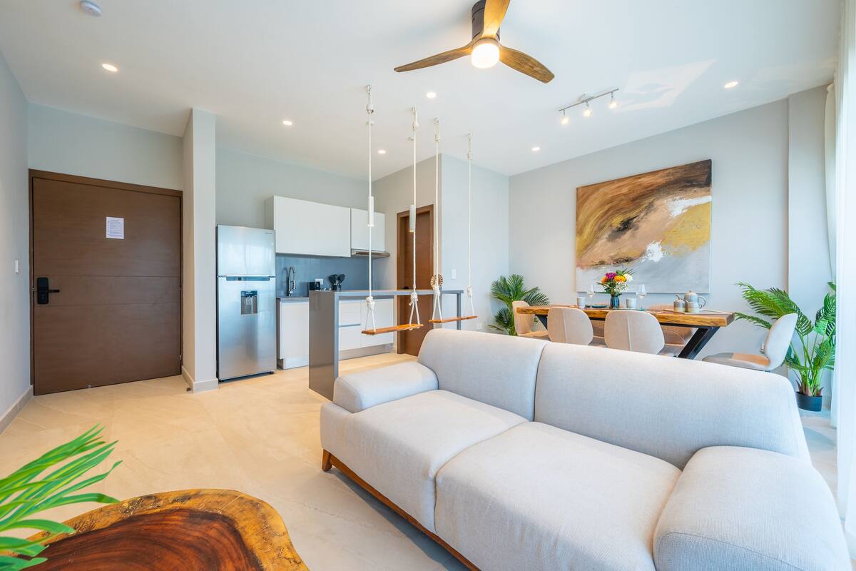 Un salon moderne comprenant un canapé, un coin repas, une cuisine et un ventilateur de plafond.
