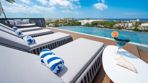 A poolside area with lounge chairs and a table with a drink and a fruit.