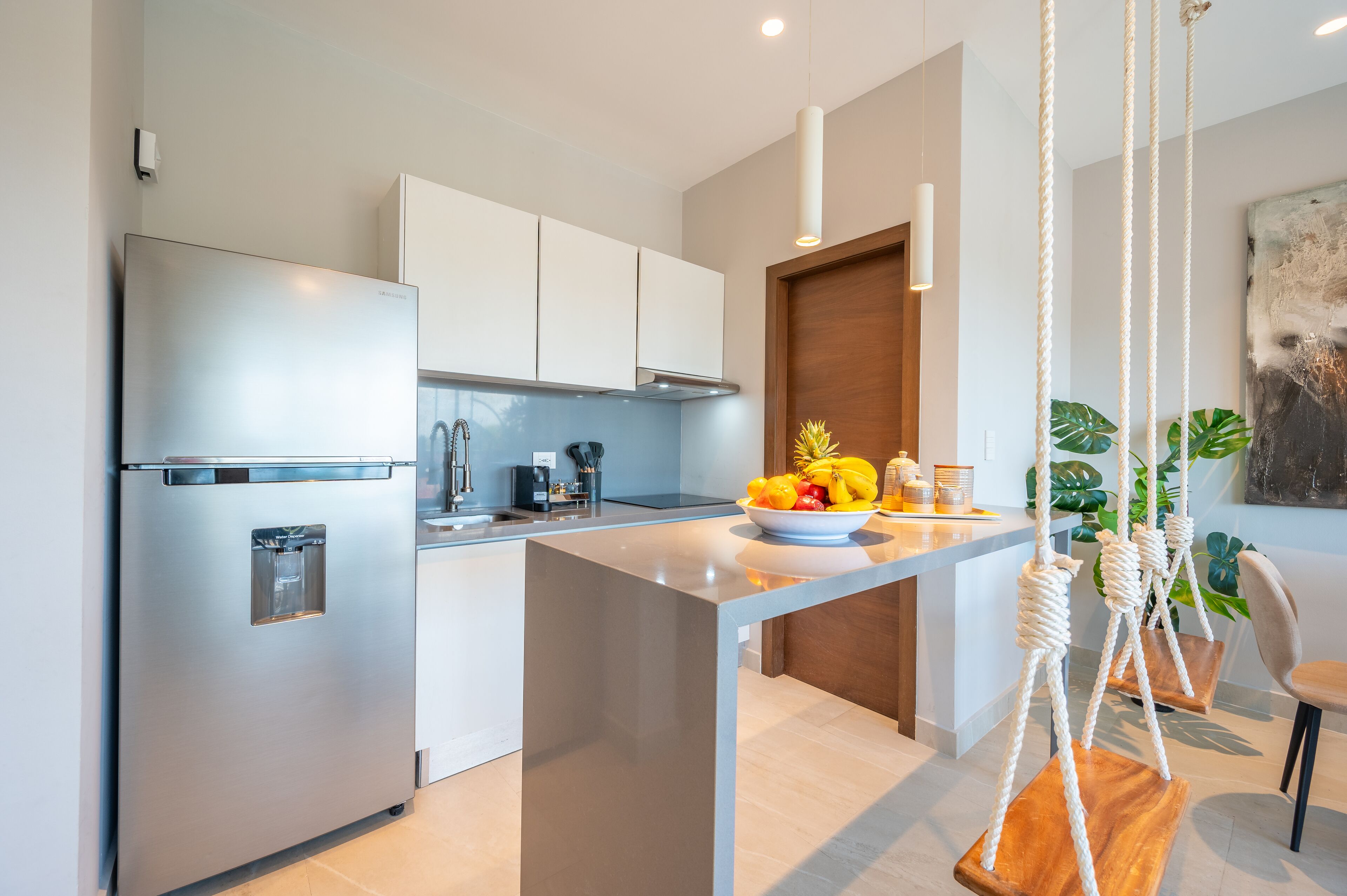 A modern kitchen with a stainless steel refrigerator, white cabinets, a wooden island, and a hanging plant.