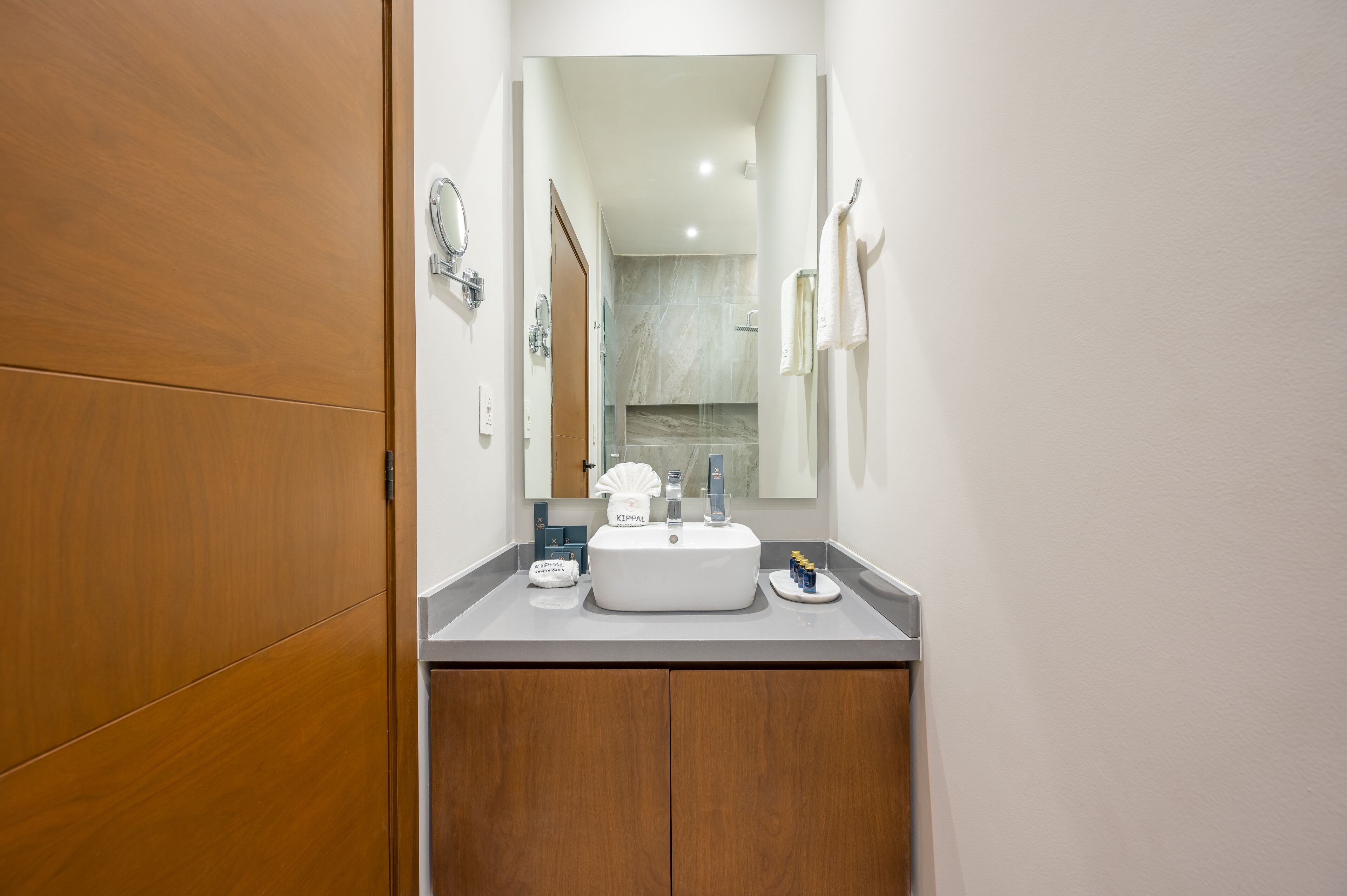 Un baño con tocador de madera, lavamanos blanco y espejo.